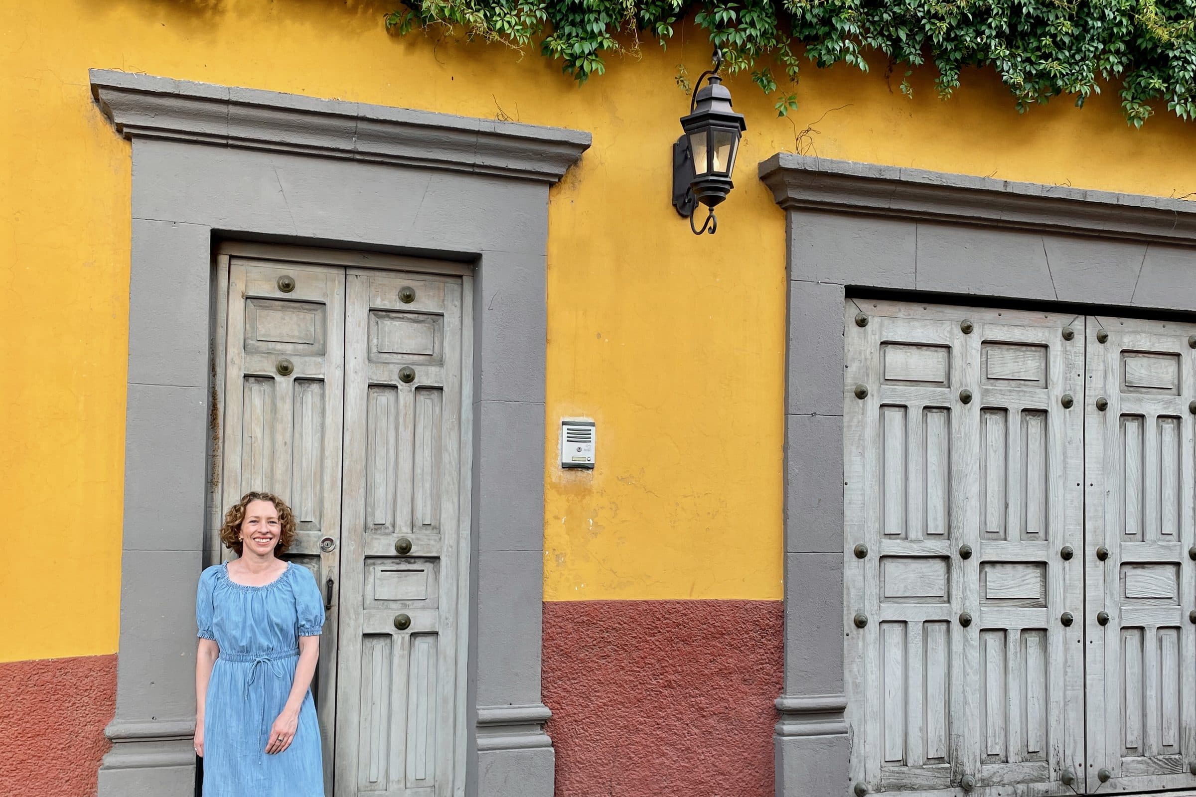 Aimee Q Devlin standing in a doorway on a yellow-walled street in San Miguel de Allende, Mexico